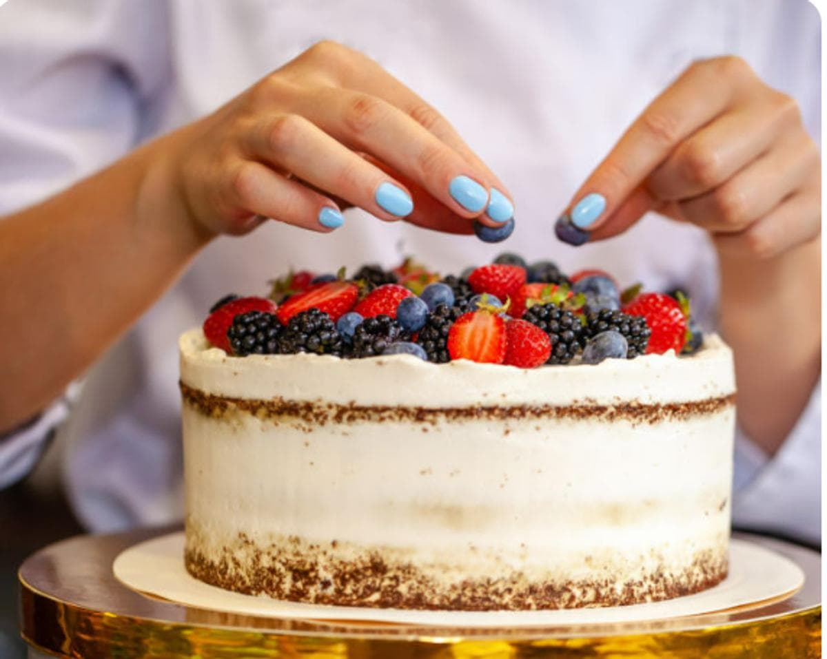 Hands decorating a fresh berry cake